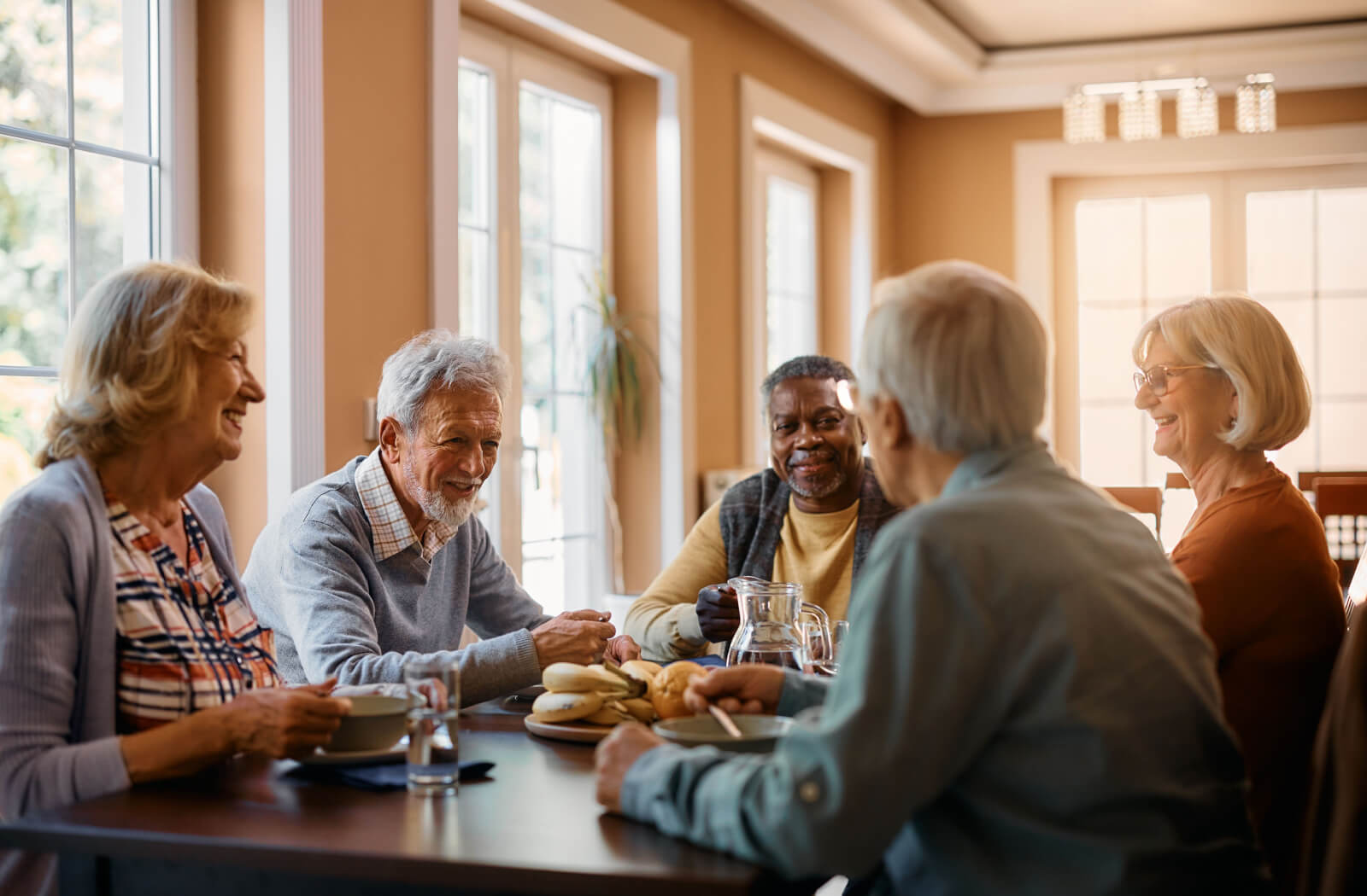 a group of seniors sit around a table chatting in a respite care community