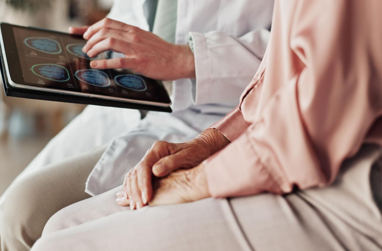A close-up of a senior's hands as they sit next to a healthcare professional, looking at scans of their brain, after experiencing dementia symptoms.