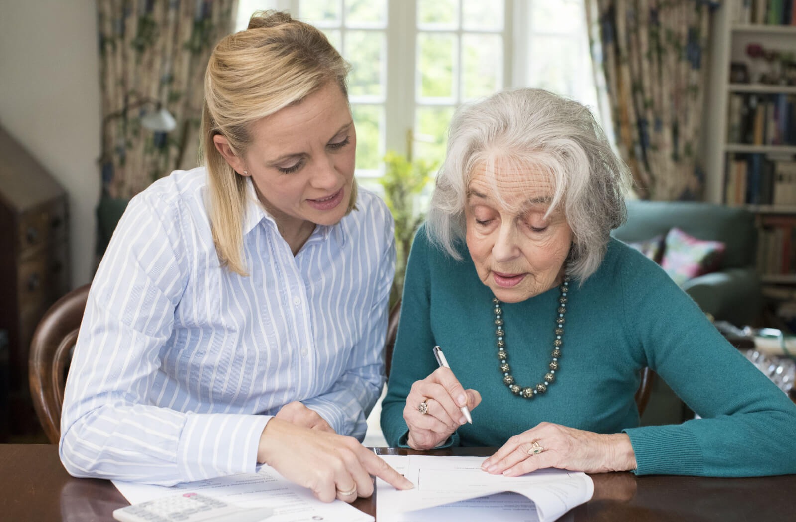 a senior and their younger child sit at a table, going over paperwork