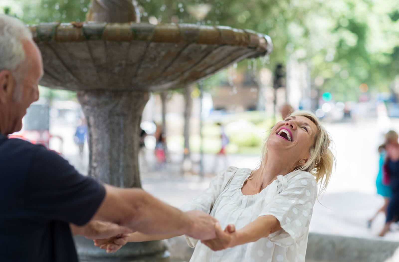 An older couple laughs while holding hands and spinning around a fountain in downtown Franklin