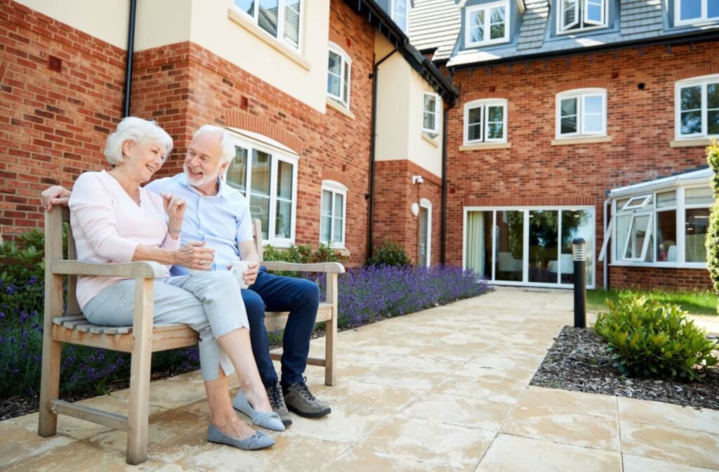 Two older adults sit on a bench together on a bench in a courtyard in memory care