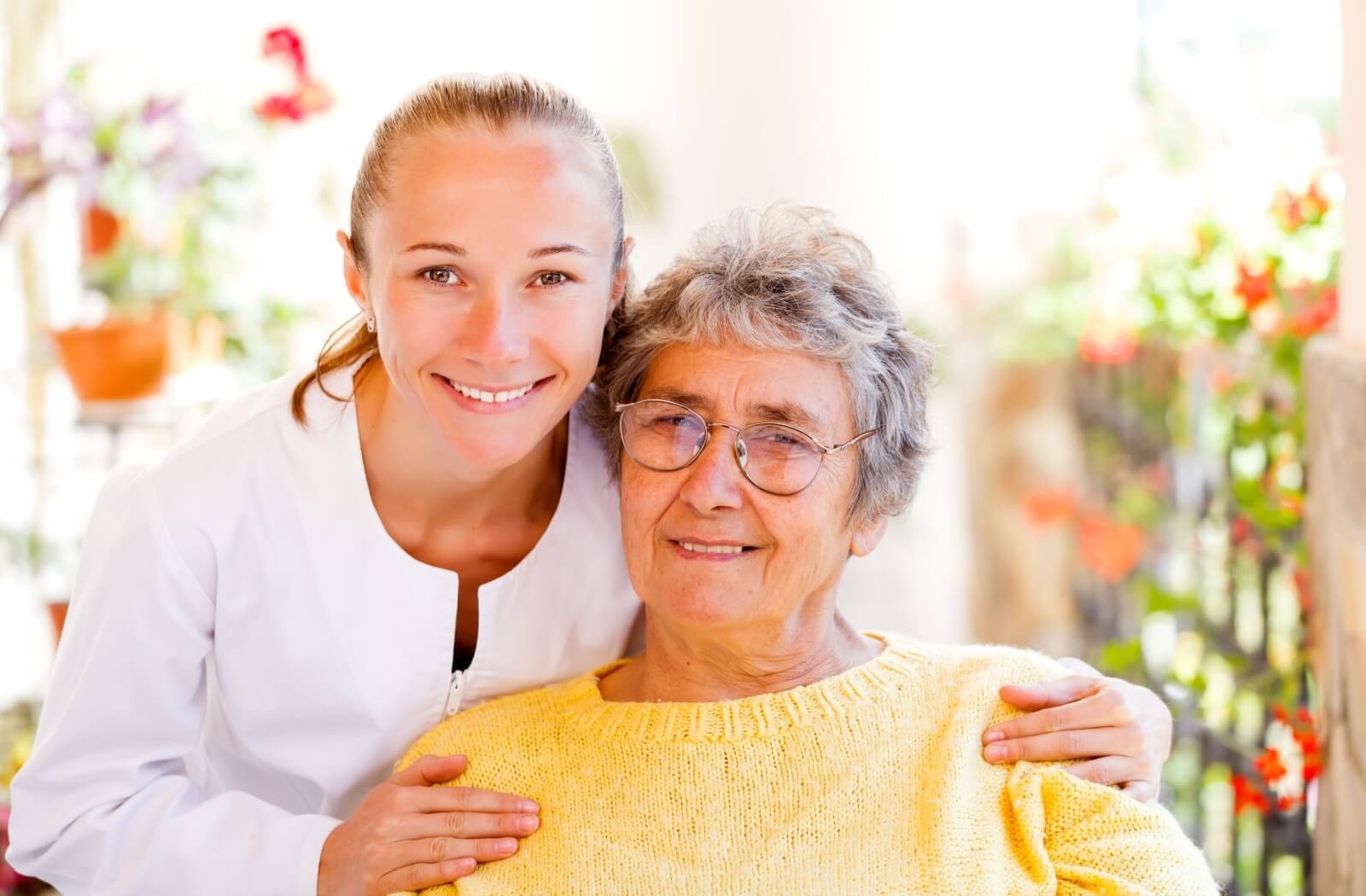 An adult child visits their smiling older parent and sits with them in a garden in memory care